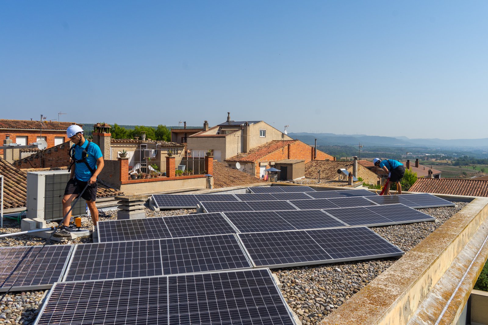 Equip de Neteja Solar netejant panells solars en teulada residencial amb poble català de fons