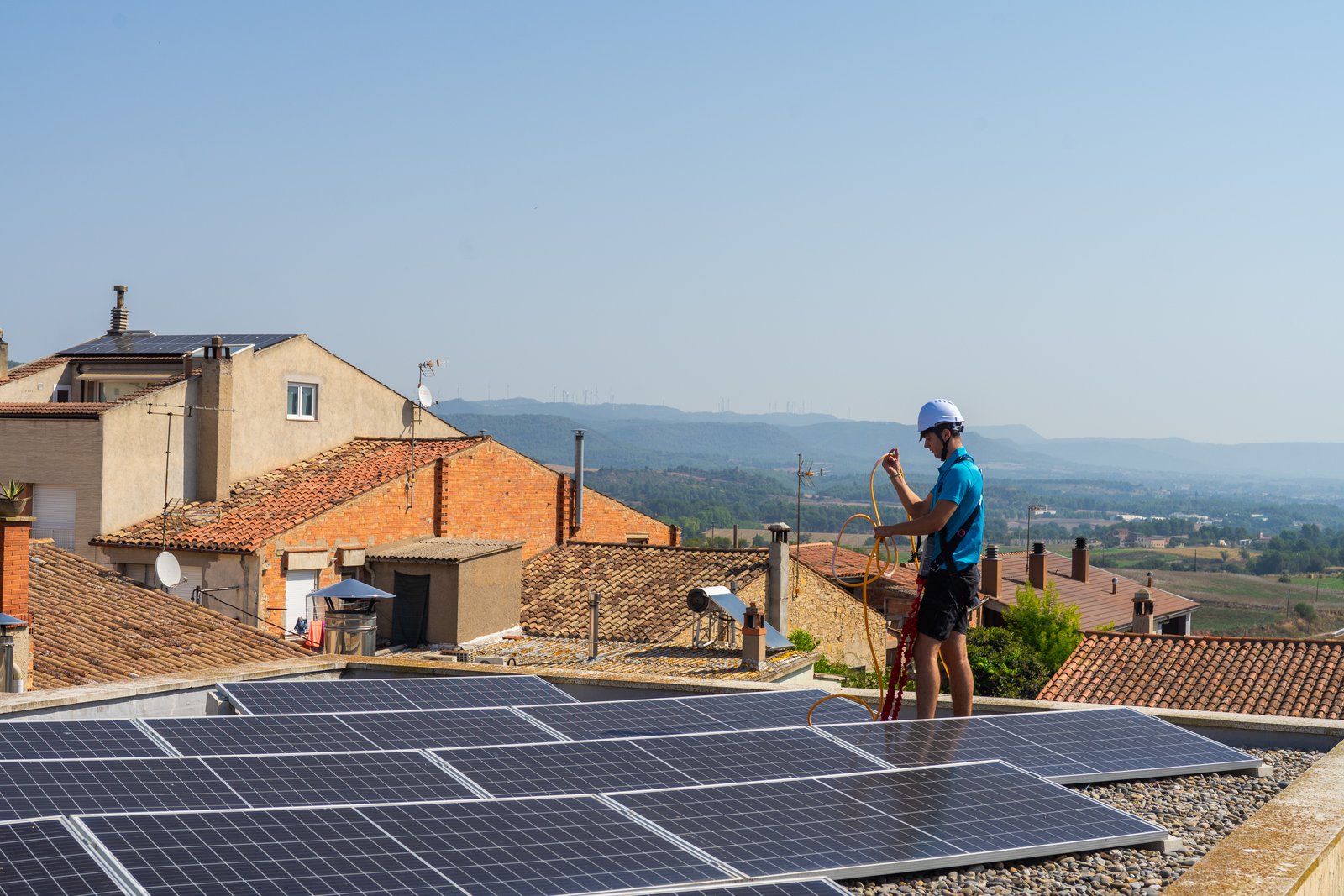 Tècnic de Neteja Solar a la teulada amb arnès de seguretat i paisatge rural