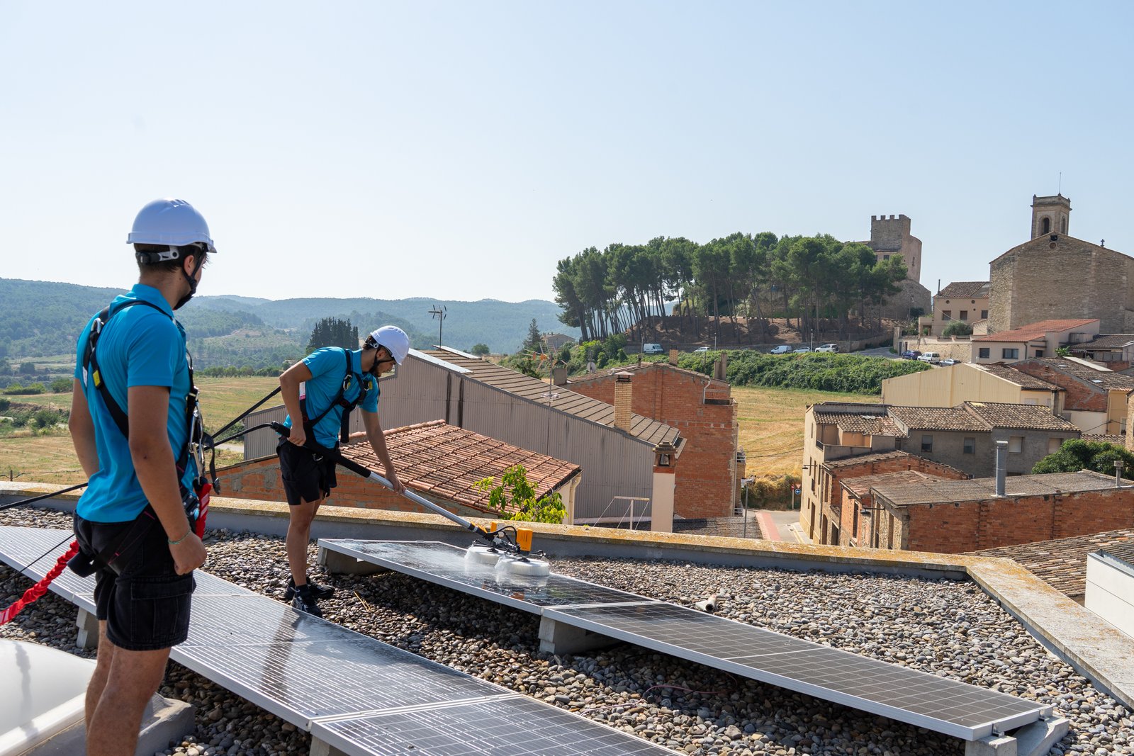 Equip de Neteja Solar netejant panells solars a teulada amb vistes a poble català